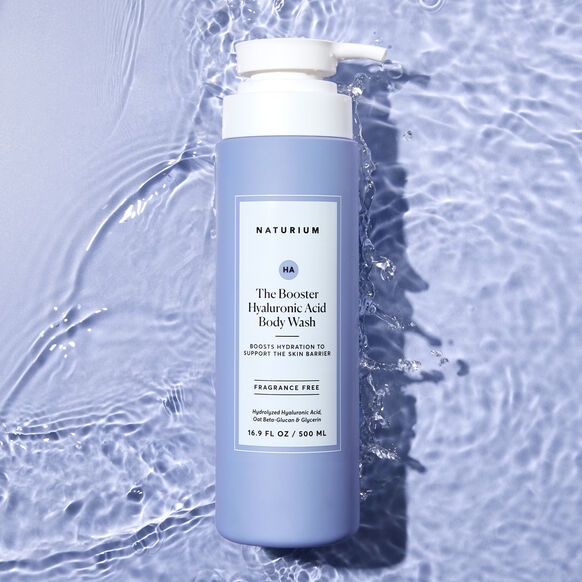 The Naturium The Booster Hyaluronic Acid Body Wash 500ml, featuring a white pump and clear label, rests on rippled light blue water with sunlit reflections. This lavender hydrating body wash is from Naturium.
