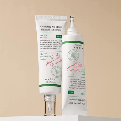 Two tubes of Axis-Y Complete No-Stress Physical Sunscreen 50ml on a beige background. Infused with mugwort and niacinamide, one tube is upright with its cap off, while the other leans diagonally, highlighting both text and elegant design. Brand: AXIS - Y.