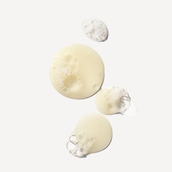 Close-up of four drops of creamy, pale yellow OLAPLEX No.4 Bond Maintenance Shampoo 100ml with bubbles on a white background, showcasing its smooth, foamy texture and bond-repairing benefits as part of the 3-4-5 Bond Maintenance System.