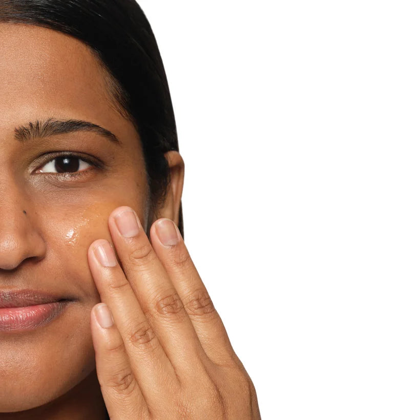A close-up shows a person with medium skin tone applying The Ordinary Niacinamide 10% + Zinc 1% serum to their cheek, ideal for blemish-prone skin, against a plain white background.