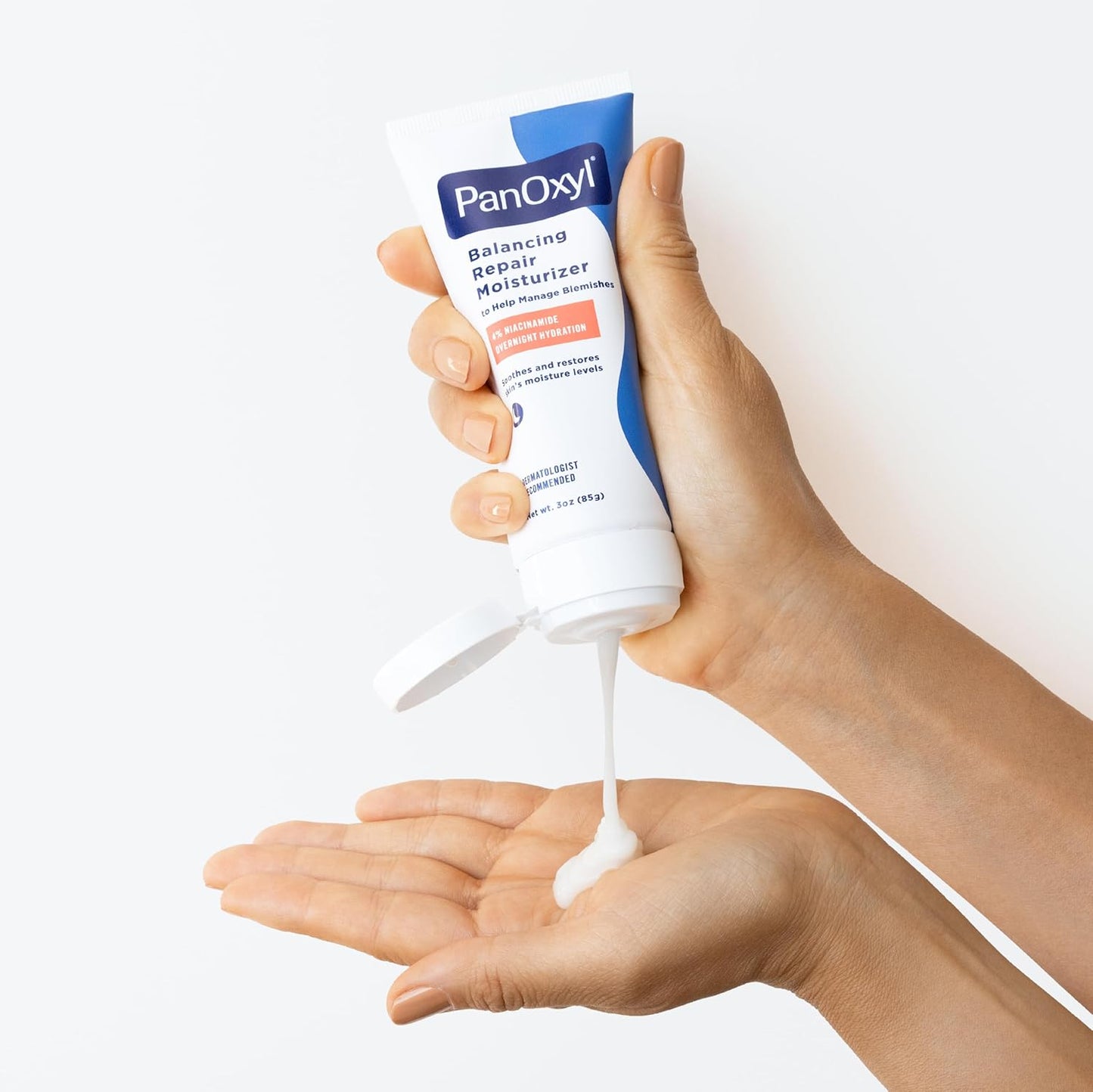 Hand holding a tube of PanOxyl Balancing Repair Moisturizer with cream being dispensed onto the palm.