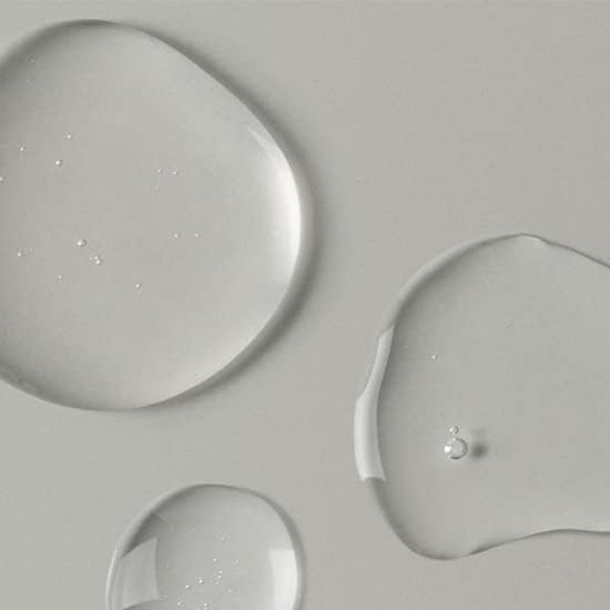 Clear liquid droplets on a smooth, light grey surface capture the essence of Abib Pore Cleansing Oil Heartleaf Oil-Wash. They vary in size and shape, contrasting the matte background with their glossy appearance, evoking a refreshing pore-clearing experience.