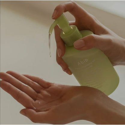 A person dispenses Abib Pore Cleansing Oil Heartleaf Oil-Wash 200ml from a light green pump bottle into their palm, with the bottle set against a soft, neutral background lit by sunlight.