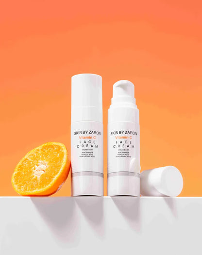 Two skincare bottles with a sliced orange on an orange background