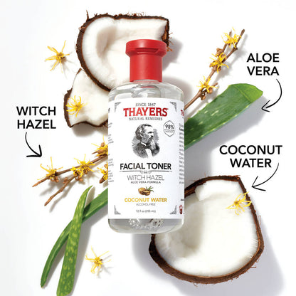 A THAYERS Facial Toner bottle is set among aloe vera leaves, coconut halves, and witch hazel twigs. The label highlights key ingredients: witch hazel, aloe vera, and coconut water. Arrows emphasize the natural elements enhancing this Coconut Water facial toner.