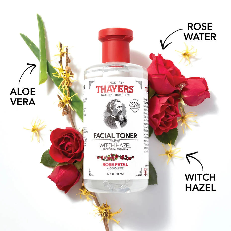 A THAYERS Facial Toner - Witch Hazel Aloe Vera Formula - Rose Petal bottle with a red cap is surrounded by aloe vera leaves, red roses, and witch hazel flowers. Arrows point to ingredients: aloe vera, rose water, witch hazel.