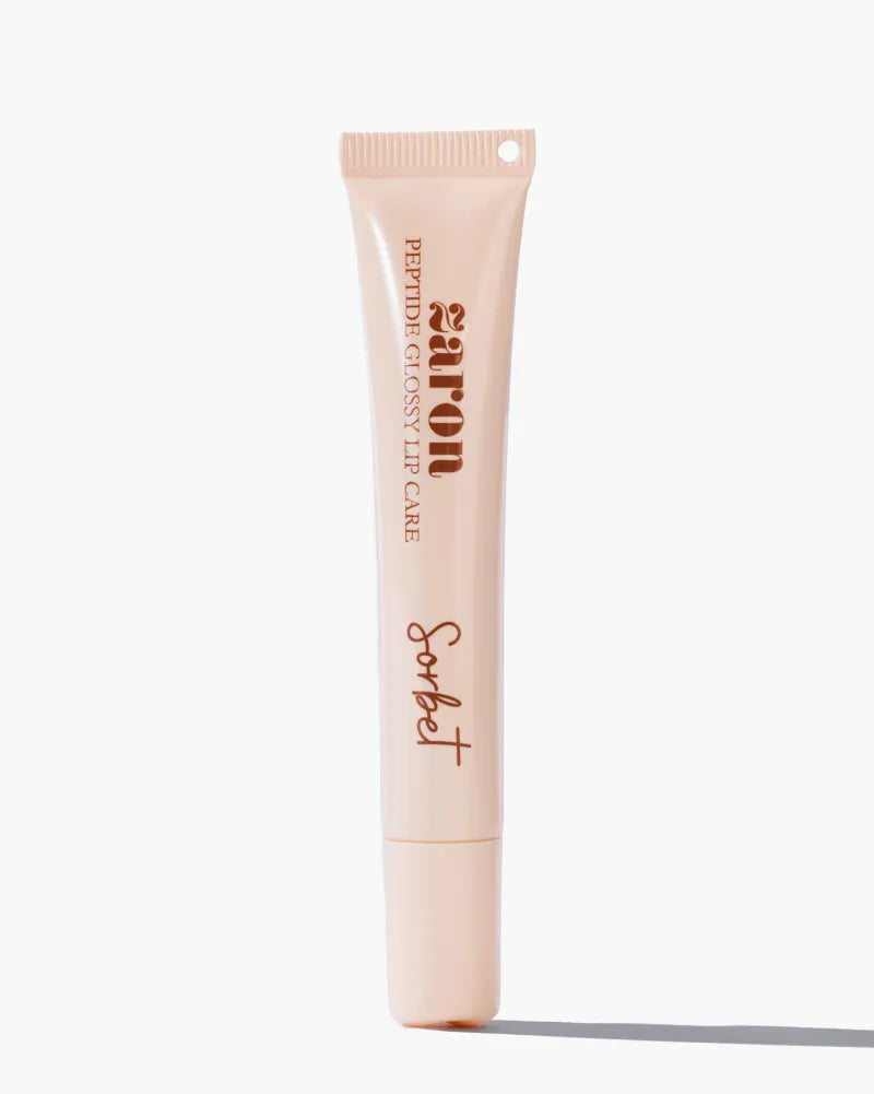 A squeeze Zaron lip glossy care in the shade 'Sorbet', featuring a pale peach-pink body with dark brown text, set against a clean white background with a soft shadow.