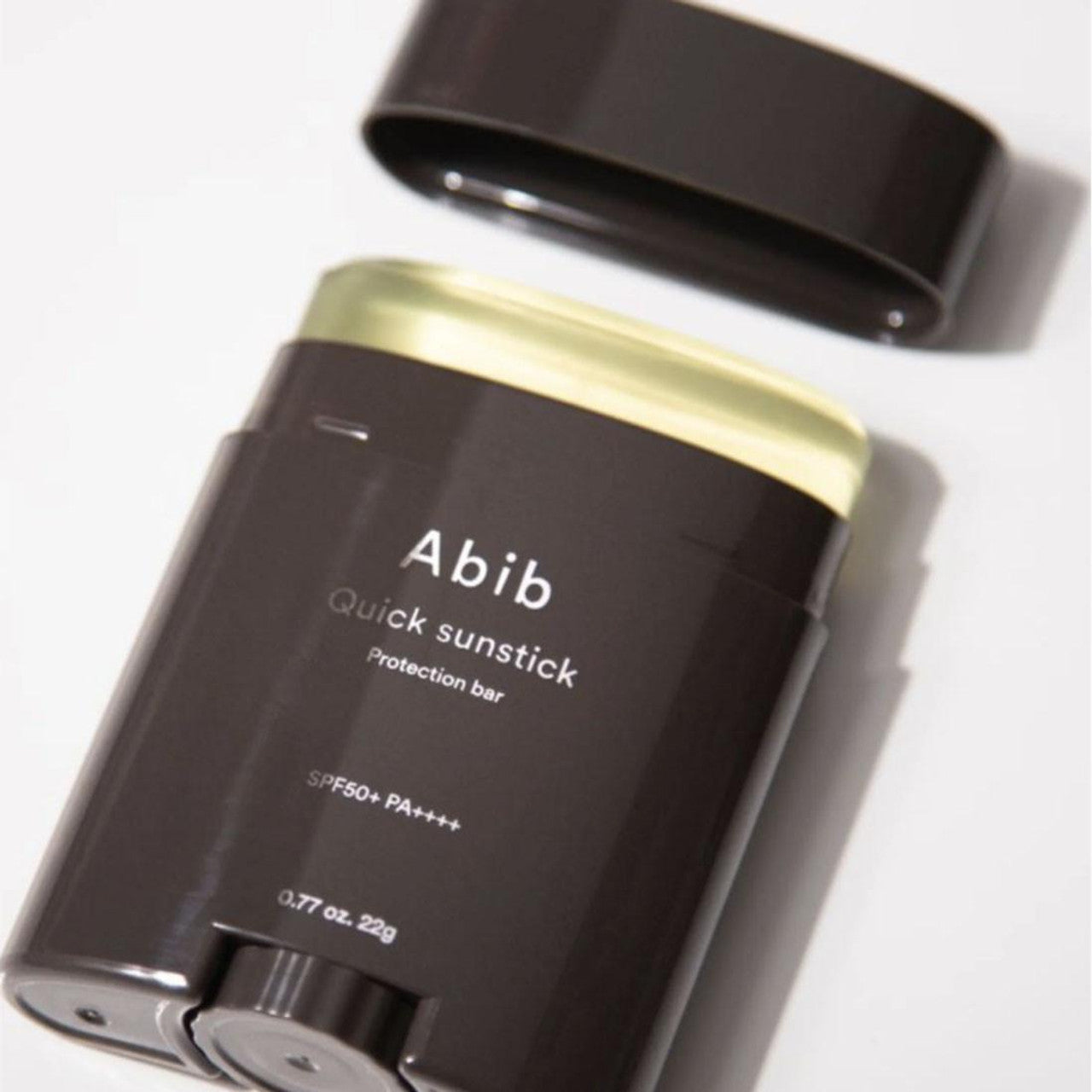 Close-up of the Abib Quick Sunstick Protection Bar SPF50+ PA++++ (22g) with its cap off in a sleek dark container, showcasing the light yellow stick that protects and strengthens your skin barrier.