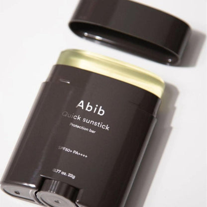 Close-up of the Abib Quick Sunstick Protection Bar SPF50+ PA++++ (22g) with its cap off in a sleek dark container, showcasing the light yellow stick that protects and strengthens your skin barrier.
