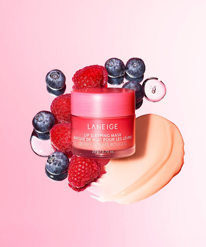 A pink jar of LANEIGEs Laneige Lip Sleeping Mask - BERRY 20g, rich in vitamin C, is surrounded by fresh blueberries and raspberries on a pink background, with a dollop of the creamy product smeared beside it to emphasize the berry fruit theme.