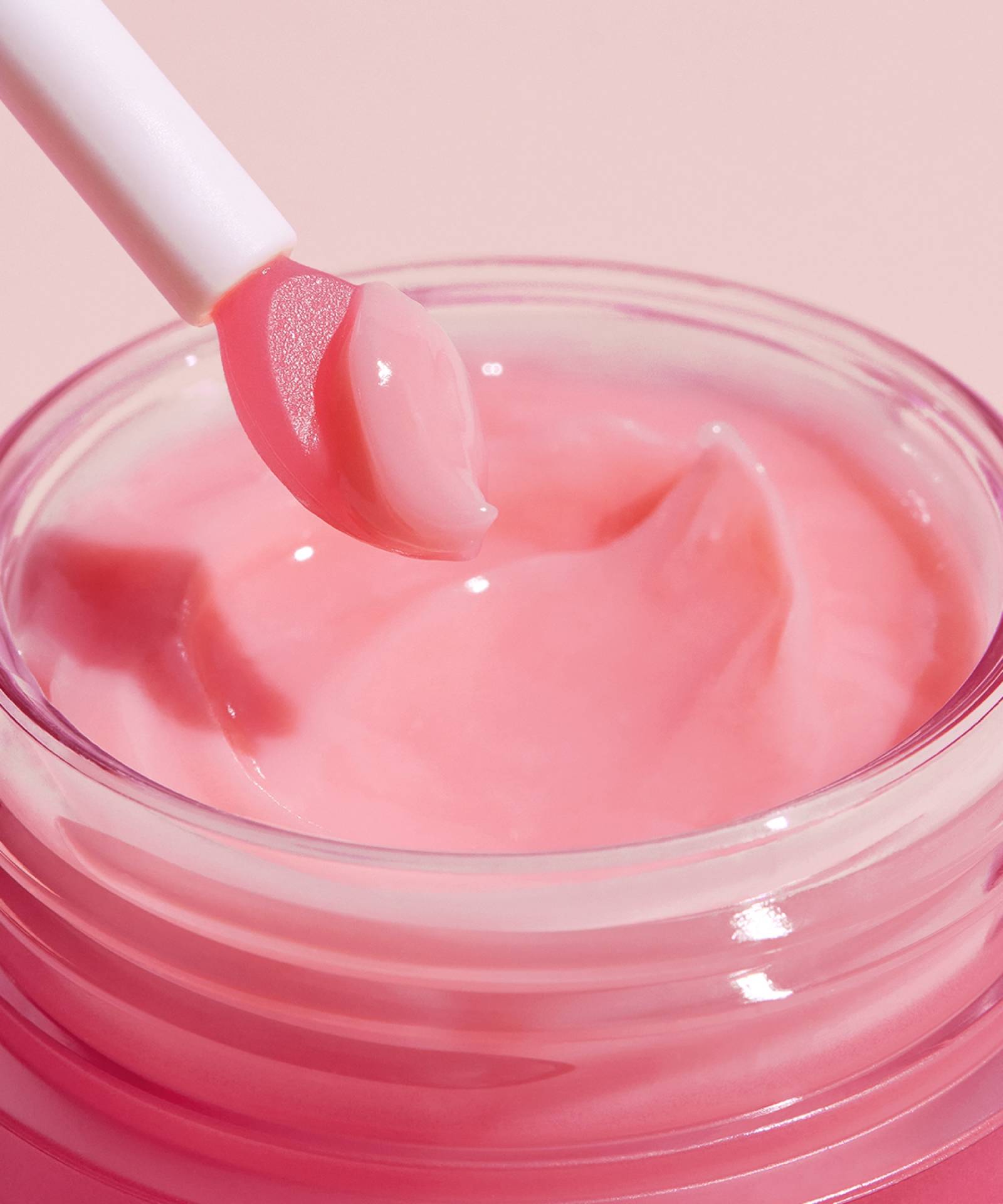 A close-up shows the Laneige Lip Sleeping Mask in BERRY 20g, featuring nourishing pink cream. A white spatula rests on the rim with a small dab. The light pink background beautifully complements this LANEIGE product, designed to revitalize your lips overnight.
