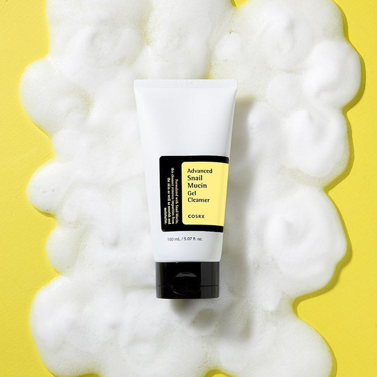 A tube of COSRX Advanced Snail Mucin Gel Cleanser (50ml) sits on a yellow surface, surrounded by foamy bubbles. The white tube features a yellow label and black cap, designed to seal in moisture while providing gentle cleansing power.