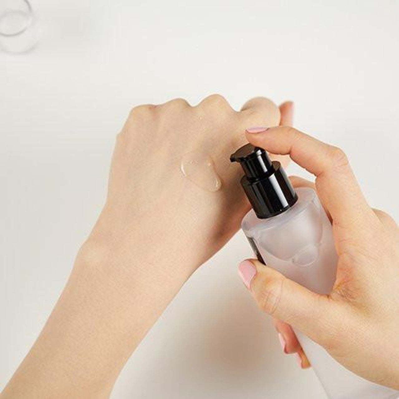 A person dispenses COSRX BHA Blackhead Power Liquid from a frosted pump bottle onto the back of their light-skinned hand against a plain, light background.