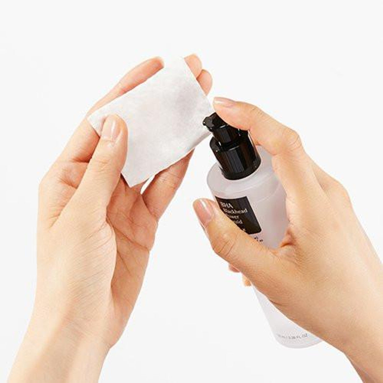 Someone is applying COSRX BHA Blackhead Power Liquid 100ml with a black pump onto a cotton pad against a plain white background. This COSRX product, featuring natural ingredients, effectively exfoliates dead skin cells for smoother, healthier-looking skin.