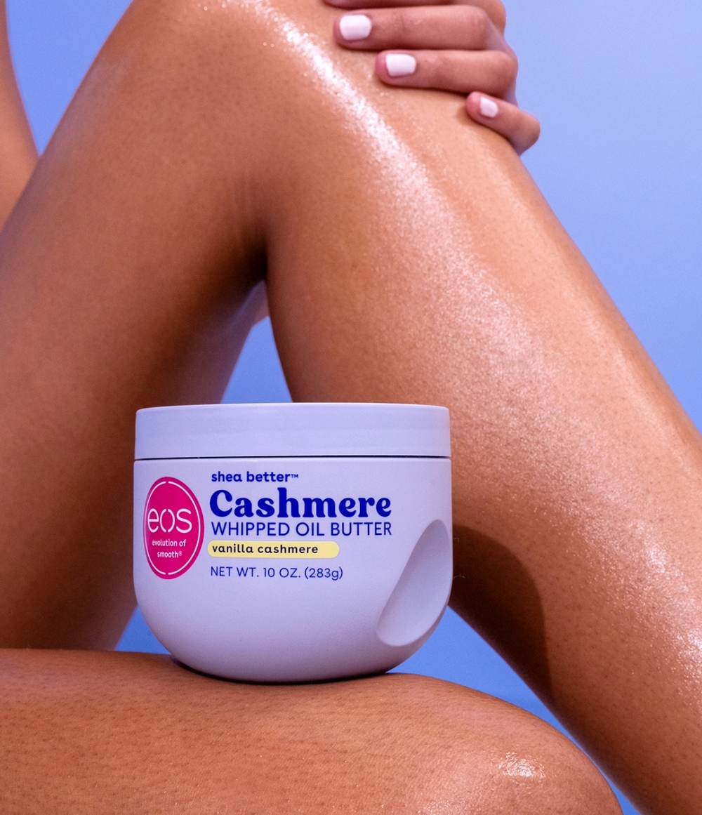 Jar of eos Cashmere Whipped Oil Butter on a person's leg with a blue background