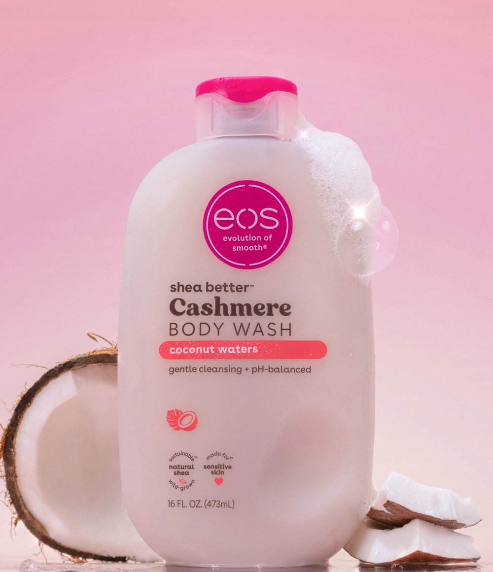 EOS Cashmere Body Wash bottle with coconut pieces on a pink background