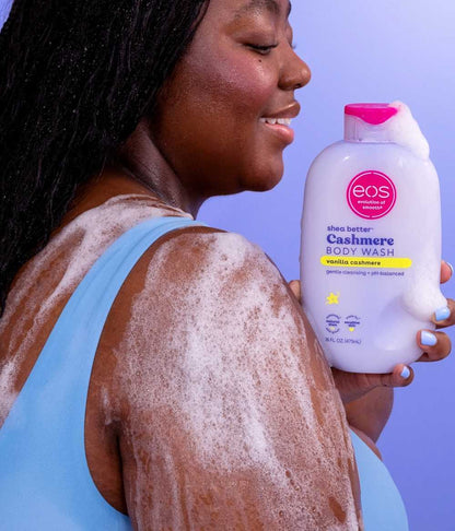 Person with foamy skin holding eos body wash bottle against a purple background