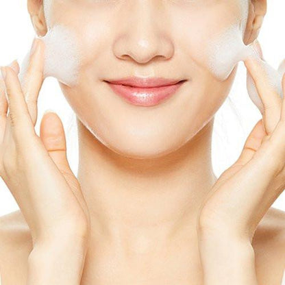 A person is gently cleansing their face with COSRX Low PH Good Morning Gel Cleanser, a vegan and cruelty-free product. They focus on the cheeks with a slight smile on smooth skin—its low pH formula enhances the experience against a plain white background, highlighting the face-washing activity.