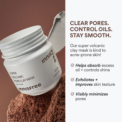 A jar of INNISFREE Super Volcanic Pore Clay Mask 100ml with a beige spatula sits on volcanic rock, highlighting benefits: effective oil control, blackhead removal, shine management, exfoliation, and improved texture for minimized pores.