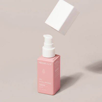 A pink bottle of Medix 5.5, 3% Hyaluronic Acid Hydrate Serum (1.7 fl oz) with a white pump appears on a beige background. Its floating white cap suggests its recently removed or about to be replaced, promising hydration enhanced by Vitamin B5.