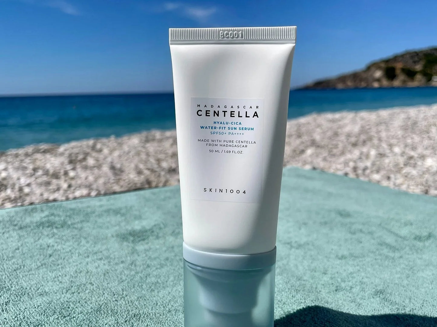 SKIN1004 Sun Serum placed outdoors by the beach, highlighting its SPF50+ PA++++ protection, lightweight texture, and moisturizing Centella Asiatica benefits