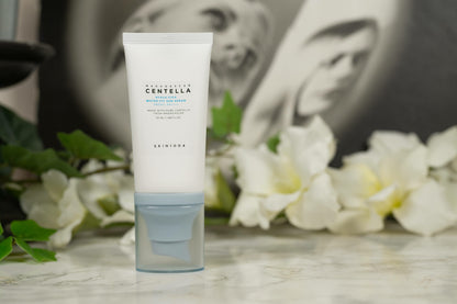 SKIN1004 Centella Sun Serum standing on a marble surface with white flowers, highlighting its SPF50+ protection and hydrating formula for all skin types