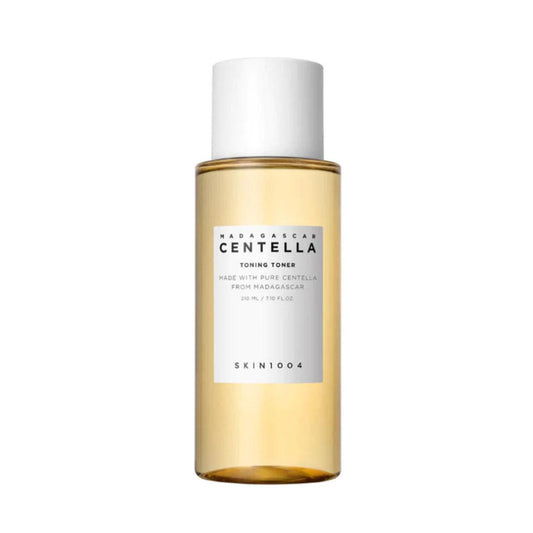 A bottle of SKIN1004 Madagascar Centella Toning Toner. The transparent bottle contains a golden-colored liquid and has a white screw cap. The label on the bottle displays the product name and description, stating it is made with pure Centella from Madagascar. The packaging is minimalist and elegant.