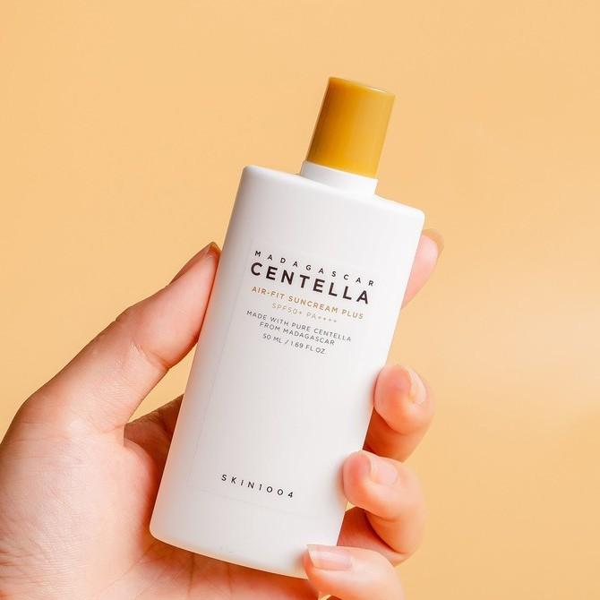 SKIN1004 Air-Fit Suncream Plus bottle held against a warm beige background, emphasizing its elegant packaging and skin-friendly UV defense formula.