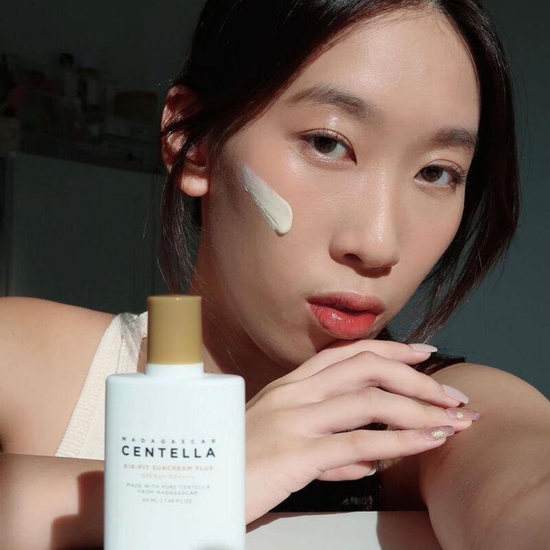 A person applying SKIN1004 Air-Fit Suncream Plus to their face, demonstrating its smooth, non-white cast formula with Centella Asiatica for soothing care