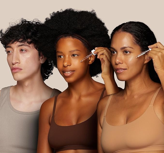 Three individuals of various backgrounds apply SKIN DEVA 20% Vitamin C + E with Ferulic Acid Serum to their faces using droppers. They stand side by side in neutral-toned tops against a beige background, highlighting the effectiveness of antioxidant skincare.