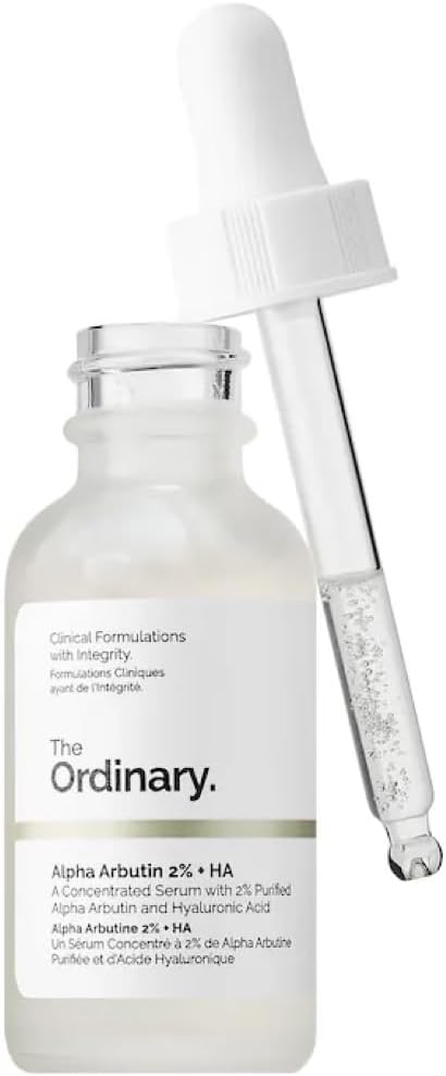 The Ordinary Alpha Arbutin 2% + HA Serum 30ml, in a clear bottle with English and French details, sits beside its dropper. The clear liquid inside is enriched with hyaluronic acid to tackle hyperpigmentation.