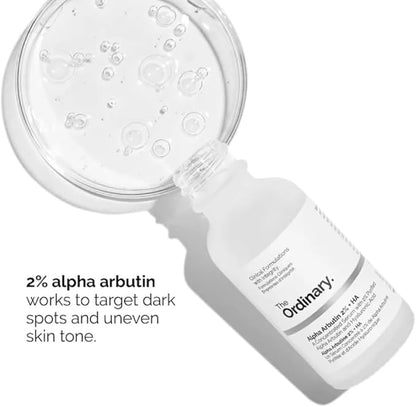 A white bottle of The Ordinary Alpha Arbutin 2% + HA Serum 30ml is beside a clear petri dish with bubbles. Text reads: 2% alpha arbutin targets hyperpigmentation and uneven skin tone.