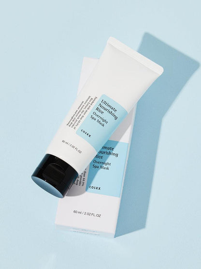 A 60ml white tube of COSRX Ultimate Nourishing Rice Overnight Spa Mask sits on its box against a light blue background. The tube has a black cap and blue label, enriched with rice extract for brightening and moisturizing, offering radiant skin benefits.