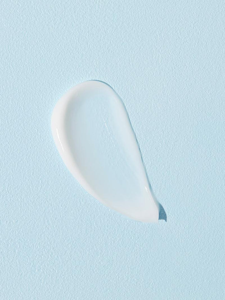 A dollop of COSRX Ultimate Nourishing Rice Overnight Spa Mask is applied on a smooth, light blue surface, creating an abstract shape. Infused with rice extract, its texture is smooth and glossy, softly reflecting light off its moisturizing surface.